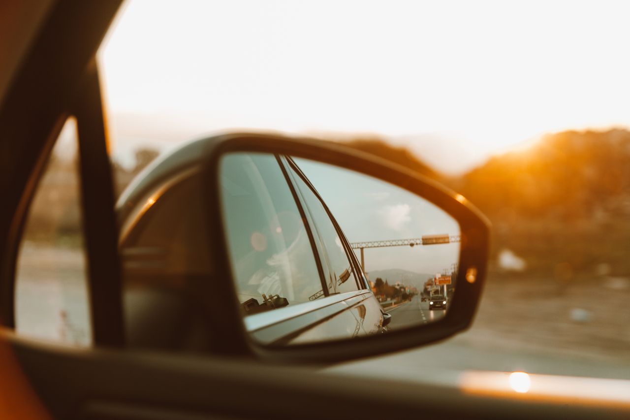 Capture of car side mirror showing a scenic sunset view during a road trip.